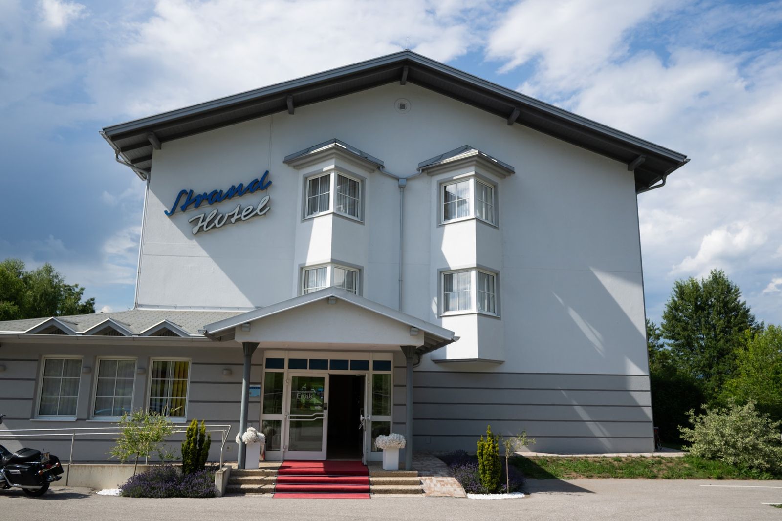 Exterior view of Strandhotel Faak on the southern shore of Lake Faak with free parking in front of the hotel
