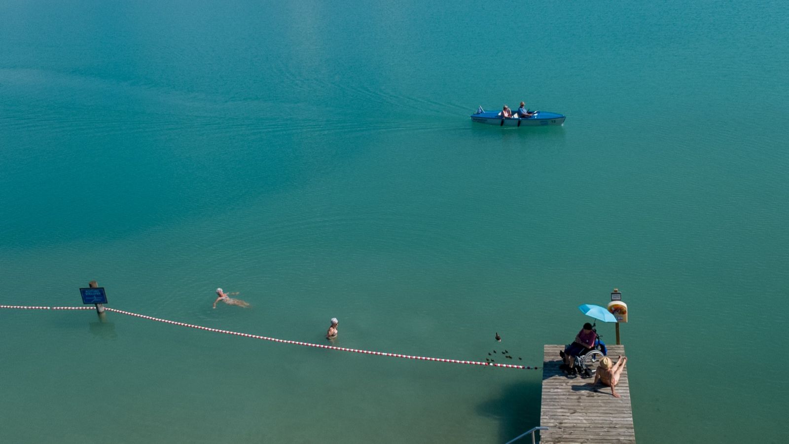 Aerial view of Lake Faak with the hotel and mountain backdrop