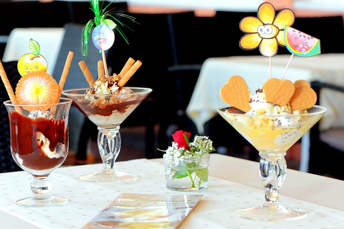 Three decorated ice-cream sundaes in glasses on the terrace